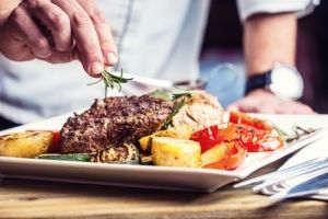 A chef is garnishing a plate with steak and potatoes